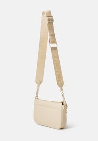 Sac bandoulière beige en matériau texturé ; dispose d'une large sangle avec des lettres gaufrées et du matériel en métal pour l'attache.
