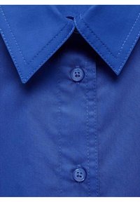 Camicia di cotone blu con un ampio colletto a punta e design con chiusura a bottoni, dotata di un bottone blu coordinato. Tessuto liscio con cuciture diagonali.