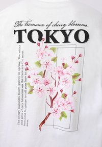 Κλαδί κερασιάς με ροζ λουλούδια και πράσινα φύλλα δίπλα στο κείμενο «Το ρομάντζο των ανθισμένων κερασιών. ΤΟΚΙΟ» σε λευκό φόντο.
