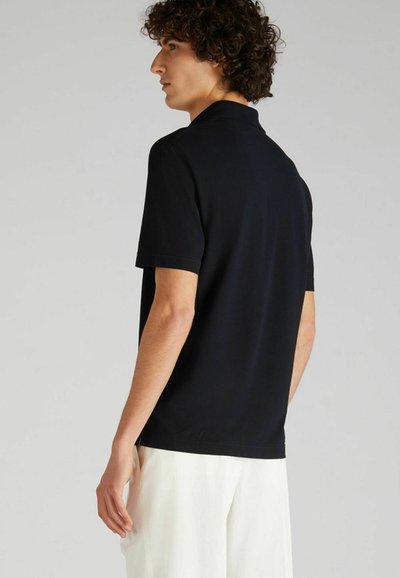 Camisa polo negra hecha de algodón suave, con un cuello clásico y mangas cortas. Textura suave con un diseño ajustado.