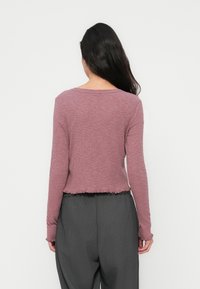 Μπλούζα μακρυμάνικη, ριμπ πλεκτή σε αποχρώση μωβ με στρογγυλή λαιμόκοψη και ξεφτισμένο τελείωμα, συνδυασμένη με φαρδιά, σκούρα γκρι παντελόνια.