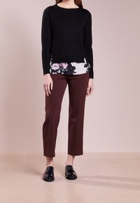 Černý dlouhý rukáv top vrstvený přes bílou květinovou blůzu, v kombinaci s hnědými vytvarovanými kalhotami a lesklými černými botami. Jednoduchý a přiléhavý design.