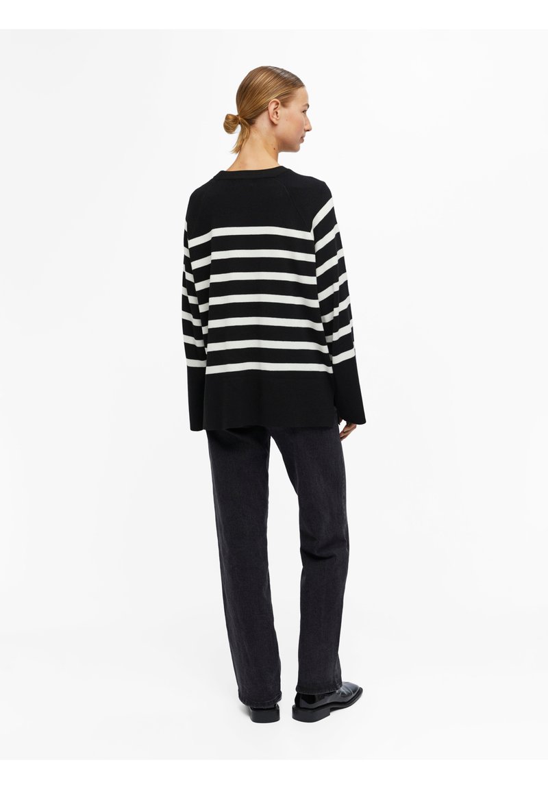 Pull rayé noir et blanc avec des manches larges et une coupe décontractée, associé à un jean en denim foncé et des chaussures noires brillantes.