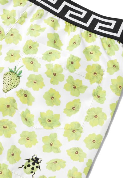 Pantaloni corti da uomo caratterizzati da un vivace tessuto bianco con motivi floreali verdi, un dettaglio con fragola e coccinella, e una cintura nera a motivo.