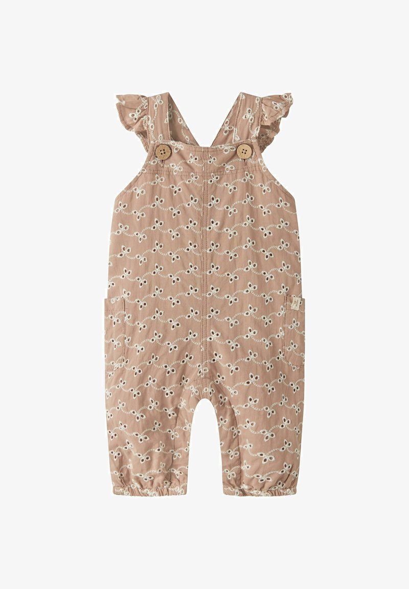 Combinaison courte couleur fauve avec broderie florale blanche, bretelles volantées, boutons en bois et poignets élastiques. Comprend des poches latérales et une coupe décontractée.