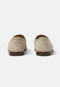 Mocasines de ante gris con punta redonda, diseño sin cordones y suela de madera marrón. Presentan sutiles detalles de costura a lo largo de la parte superior.