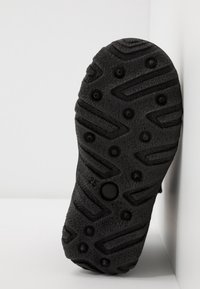 Svart gummisul med mönstrad botten, med upphöjda cirkulära och kantiga mönster för grepp. Kanterna är något slitna.