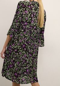 Robe noire à fleurs avec des fleurs violettes et des feuilles vertes, à manches trois-quarts et à ourlet évasé, fabriquée en tissu léger.