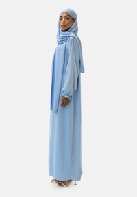 Abaya bleu clair en tissu semblable à de la soie, présentant des manches longues, un design fluide et un hijab assorti.