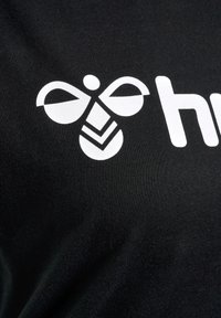 Schwarzes T-Shirt mit einem weißen stilisierten Bienenmotiv über dem Text "hive", aus einem glatten Baumwollstoff. Das Design ist gewagt und schlicht.