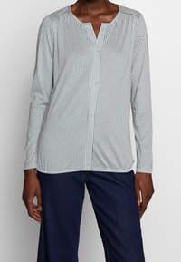 Camicia a maniche lunghe con colletto realizzata in tessuto leggero, caratterizzata da un motivo geometrico in tonalità scure e chiare. Design a V, vestibilità comoda.