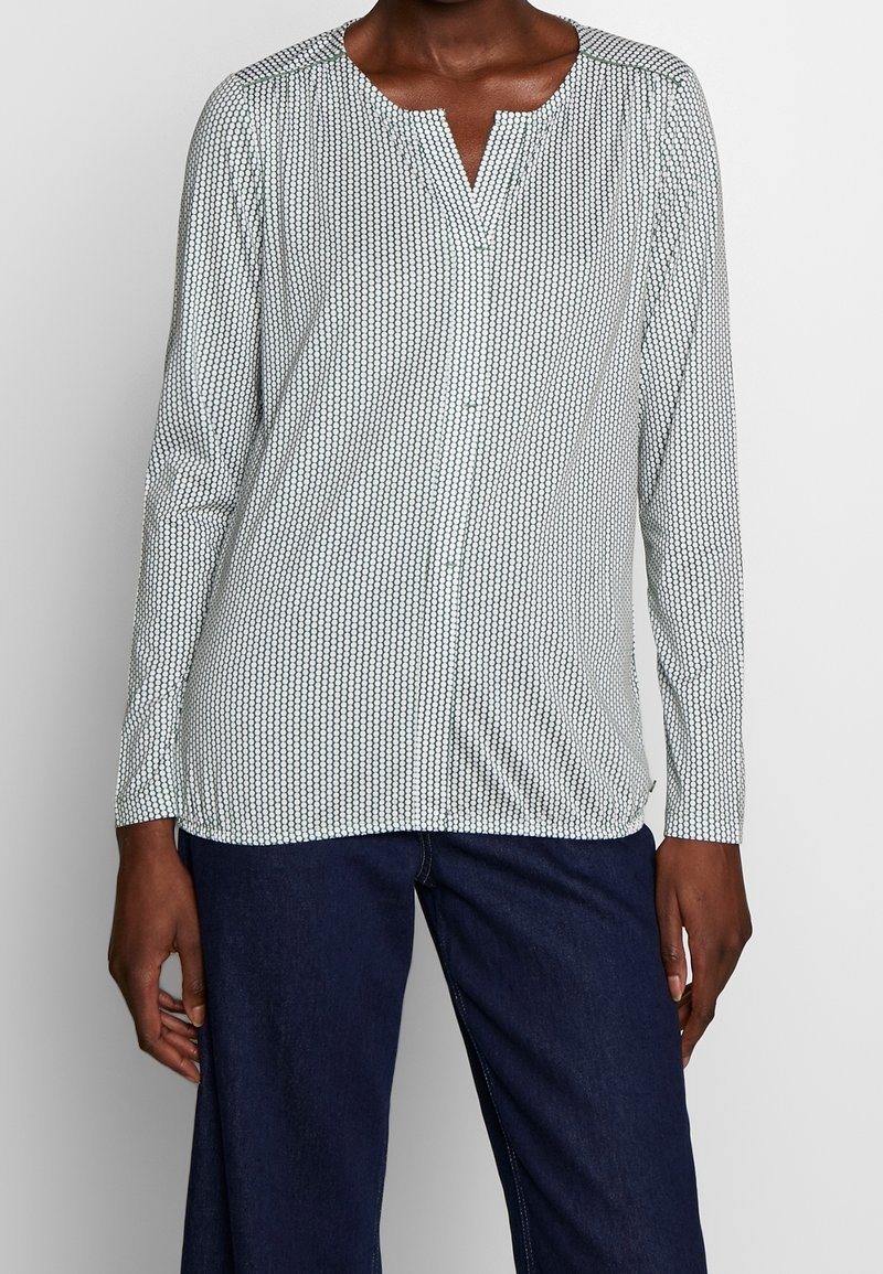 Camicia a maniche lunghe con colletto realizzata in tessuto leggero, caratterizzata da un motivo geometrico in tonalità scure e chiare. Design a V, vestibilità comoda.