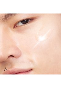 Primo piano di una guancia con una goccia lucida di siero trasparente applicata vicino all'occhio, che mette in risalto la texture della pelle liscia.