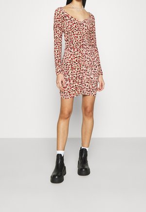 Vestido ajustado de manga larga en rojo y crema con un patrón floral. Escote en V, detalles fruncidos y combinado con botas negras hasta el tobillo.