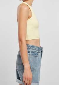 Żółty prążkowany crop top z wysokim dekoltem, zestawiony z jasnoniebieskimi szortami dżinsowymi z podwiniętymi nogawkami i tylnymi kieszeniami.