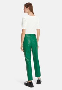 Weißes kurzärmliges T-Shirt, kombiniert mit glänzenden, grünen Kunstlederhosen mit Seitentaschen und einem dezenten Logodesign auf der Rückseite.