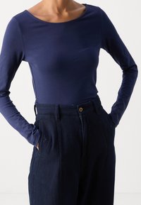 Haut à manches longues bleu marine en tissu doux avec un décolleté dégagé, associé à un pantalon large texturé foncé doté d'un bouton et de poches latérales.