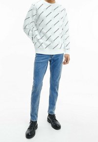 Felpa bianca con testo nero ripetuto, abbinata a jeans blu. Stivali neri con lacci completano l'outfit. Design minimalista e stile casual.