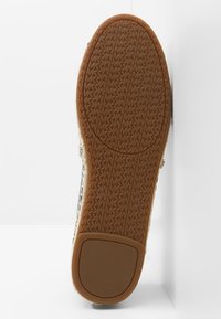 Semelle d'une sneaker, avec une surface en caoutchouc brun texturé et un motif circulaire ainsi qu'un logo en relief. Le bord montre un matériau de couleur claire.