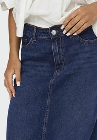 Jeans i mörkblå denim med hög midja, utrustade med knäppning framtill, subtila sömmar och en slät yta.