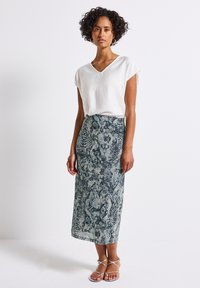 White V-neck top paired with a textured, mid-length skirt featuring a blue and green snake print pattern. Silver strappy sandals complete the look.