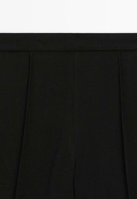 Primo piano di un tessuto nero con cuciture verticali e una cintura larga, probabilmente parte di pantaloni su misura o di una gonna.