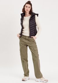 Black puffer vest, cream knit sweater, olive green cargo pants, and white sneakers. Featuring a zip closure and side cargo pockets.