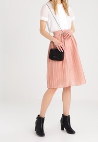 Blusa bianca leggera a maniche corte, gonna midi plissettata rosa pastello, borsa a tracolla nera con perline e stivaletti neri alla caviglia.