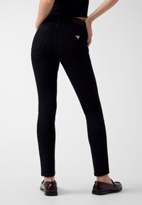 Jeans skinny neri, tessuto denim, due tasche posteriori, dettaglio logo sulla tasca, texture liscia, abbinati a mocassini scuri.