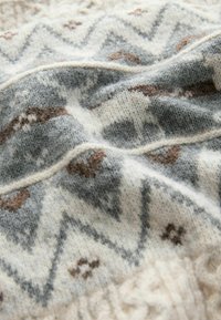 Wollpullover mit strukturierter Oberfläche, der ein Zickzackmuster in Grau-, Weiß- und Brauntönen aufweist, was ein gemütliches, geschichtetes Aussehen verleiht.