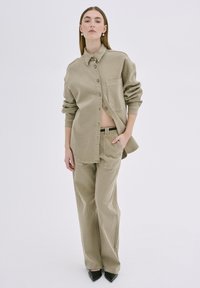 Khaki srajca s gumbi in žepom na prsih, v kombinaciji s širokimi hlačami. Gladka bombažna tekstura, eleganten dizajn in ostri črni petki.
