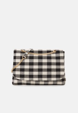 Sac à main à carreaux noir et blanc avec une bandoulière en chaîne dorée et un détail en boucle de tissu sur fond blanc.