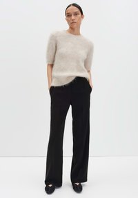 Pull en beige clair et duveteux à manches courtes, associé à un pantalon noir à jambes droites. Les chaussures sont noires avec des détails froncés.