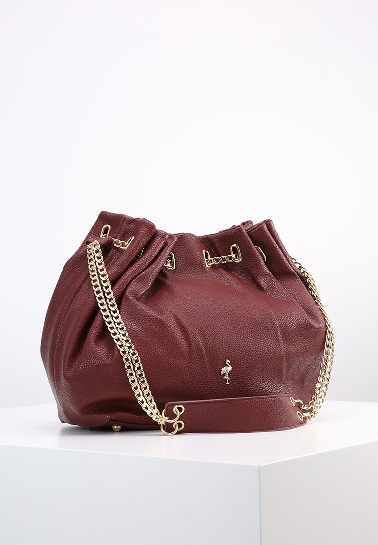 Burgundowa skórzana torba z złotymi łańcuszkami, zebranym wzorem i metalicznym akcentem w postaci logo. Teksturowana powierzchnia nadaje jej charakterystyczny wygląd.