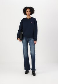 Felpa in cotone blu navy con collo rotondo e patch con logo, abbinata a jeans in denim svasati e stivaletti neri con tacco.