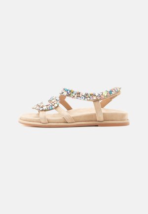 Beige flad sandal med to remme prydet med flerfarvede ædelsten, åben tå og en polstret sål på hvid baggrund.