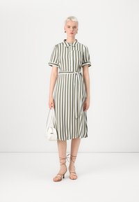 Ribade dress rohelise ja valge triibuga, lühikesed varrukad, nööbiga esiosa, vöötatud talje, põlve pikkus, koos väikese valge käsipagasi ja rihmadega sandaalidega.