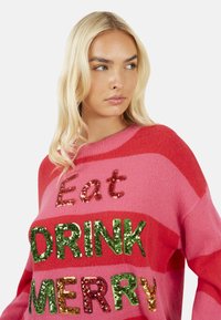 Maglione lavorato a maglia a righe rosa e rosse con testo in paillettes "Mangia BEVI FELICE." Collo a costine e vestibilità leggermente ampia. Tessuto morbido.