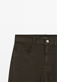 Jean en denim vert olive foncé avec poche avant, passants de ceinture, fermeture éclair et bouton argenté.