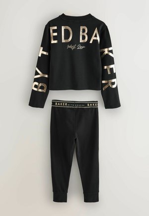 Černý bavlněný relaxační set zahrnující zkrácený top s dlouhým rukávem a legíny, ozdobený metalickým zlatým textem na přední straně a rukávech.