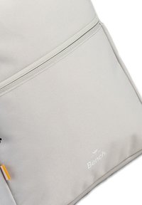 Lichtgrijze rugzak van gestructureerde stof. Heeft een voorste ritsvak, een reliëflogo en een ritslip met accentkleur.