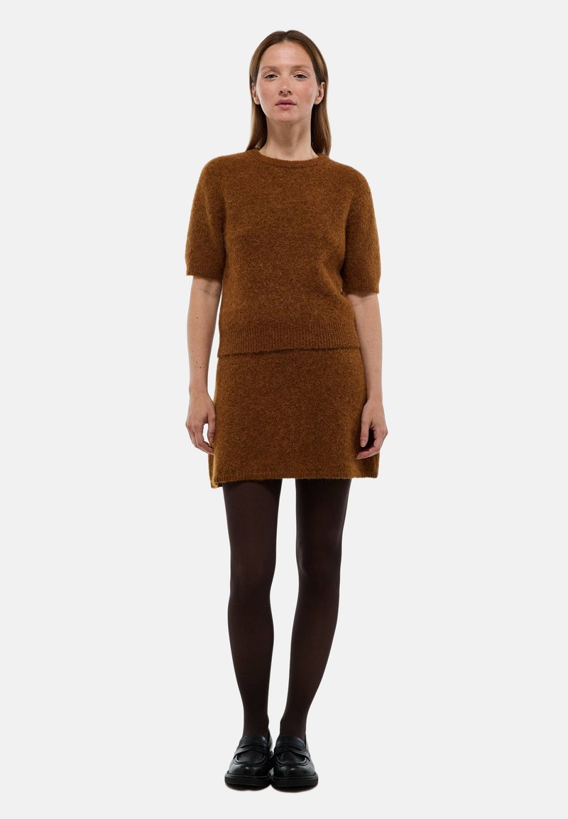 Ensemble de pull et jupe tricotés en marron, fabriqué dans un tissu doux et texturé. Manches courtes et design ajusté, associé à des chaussures noires.