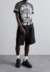 Kortärmad grafisk t-shirt i svart och grått med utsmyckad vit tryck, tillsammans med svarta shorts och svarta sneakers med vita accenter.