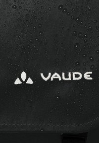 Tessuto impermeabile nero con gocce d'acqua, caratterizzato da un logo ricamato bianco "VAUDE" e un elemento di design triangolare.