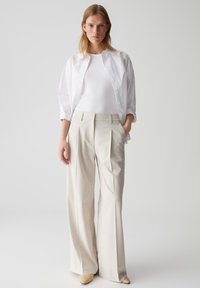 Camicia bianca a bottoni sopra un top bianco aderente, abbinata a pantaloni beige a gamba larga e tacchi a punta beige, con pieghe sottili.