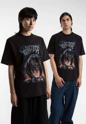 T-shirt en coton noir avec un graphisme représentant un panthère rugissante aux yeux rouges, entourée de crânes et d'un fond de fumée orange.
