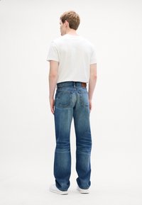 Denim jeans srednje modre barve, ravne kroj, z dvema zadnjima žepoma in rjavim usnjenim ovratnikom na pasu. Bel majica, oblečena zgoraj.