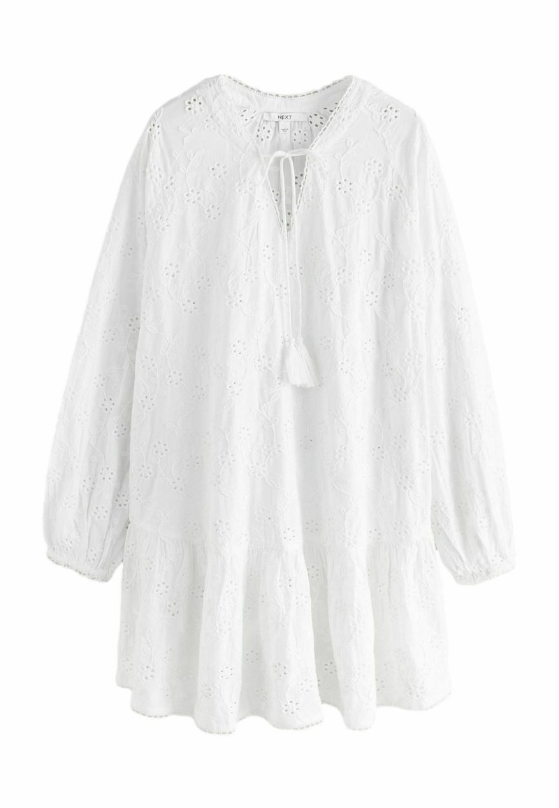 Blouse blanche à manches longues avec un ourlet à volants, ornée de broderies florales, avec un col en cœur à nouer et un tissu texturé.