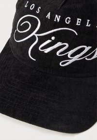 Boné preto com aba curva, apresentando texto bordado em branco que diz "Los Angeles Kings" em uma fonte decorativa. Tecido texturizado.