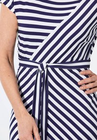 Gestreiftes Kleid in Marineblau und Weiß mit kurzen Ärmeln, Wickeldesign und einem Stoffgürtel, der in der Taille gebunden ist. Gleiche Textur erkennbar.